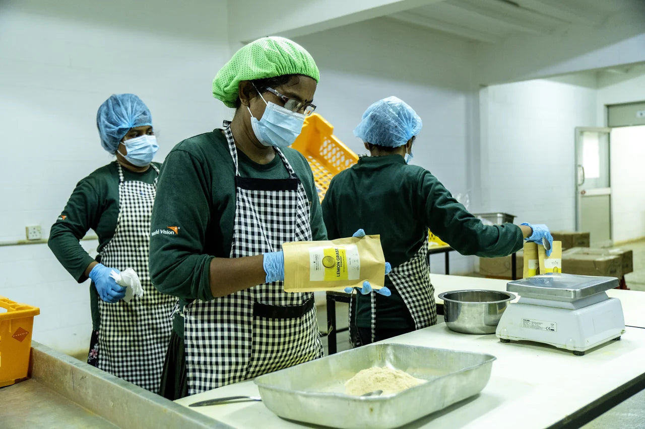 Drei Mitarbeiterinnen in Schutzkleidung prüfen fertige MrCOLOMBO Lemon Grass Pulver-Tüten in der Verarbeitungshalle Sri Lanka